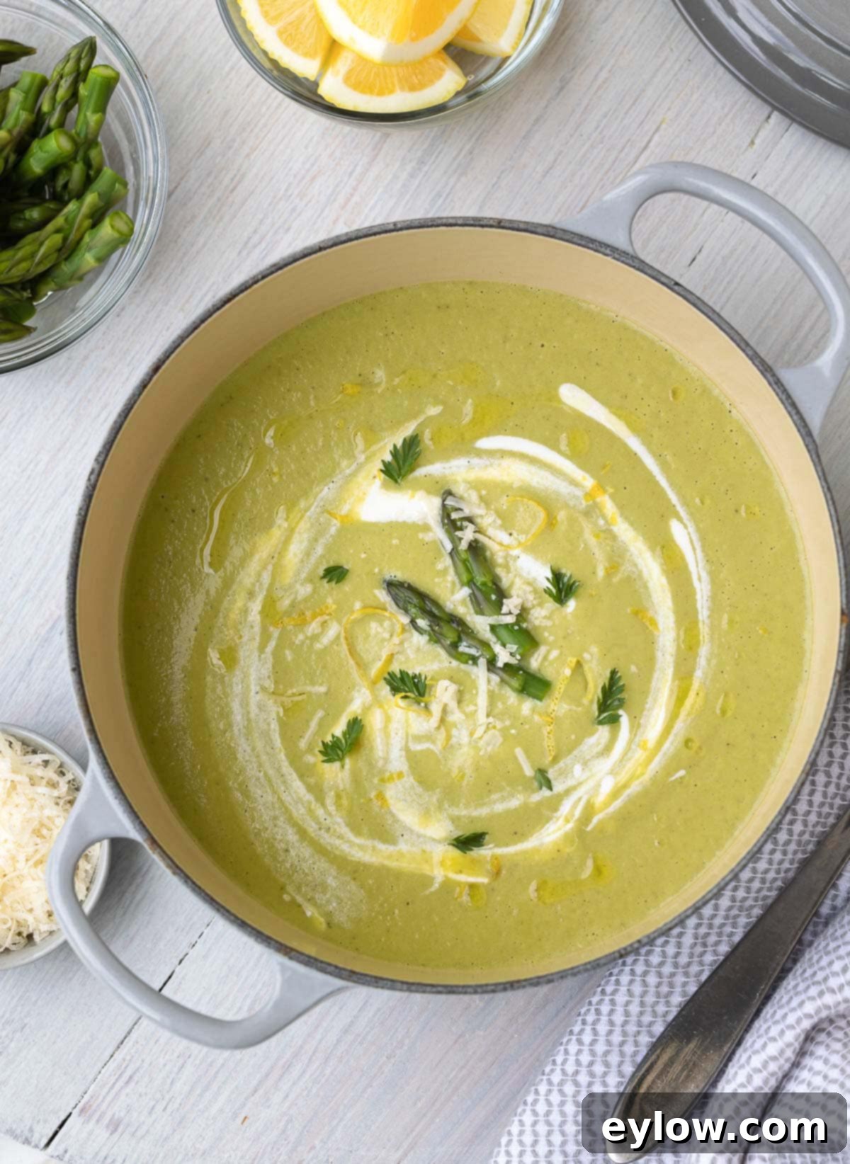 Bright green and creamy asparagus soup in a gray pot with garnishes, symbolizing fresh spring flavors.