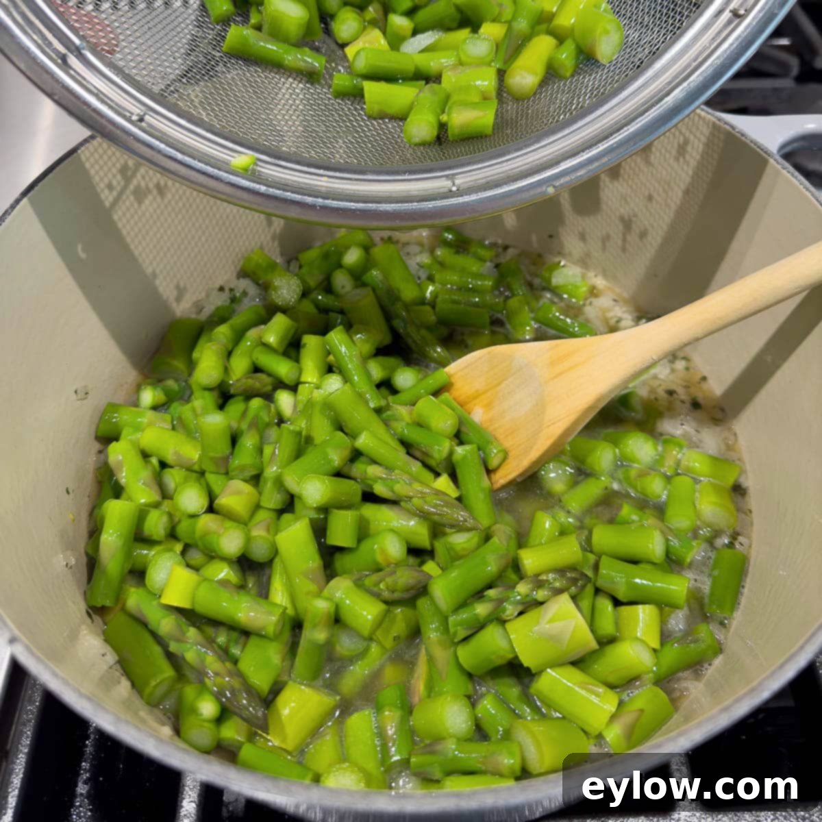 Adding cooked asparagus pieces into a pot to simmer with other ingredients for soup.