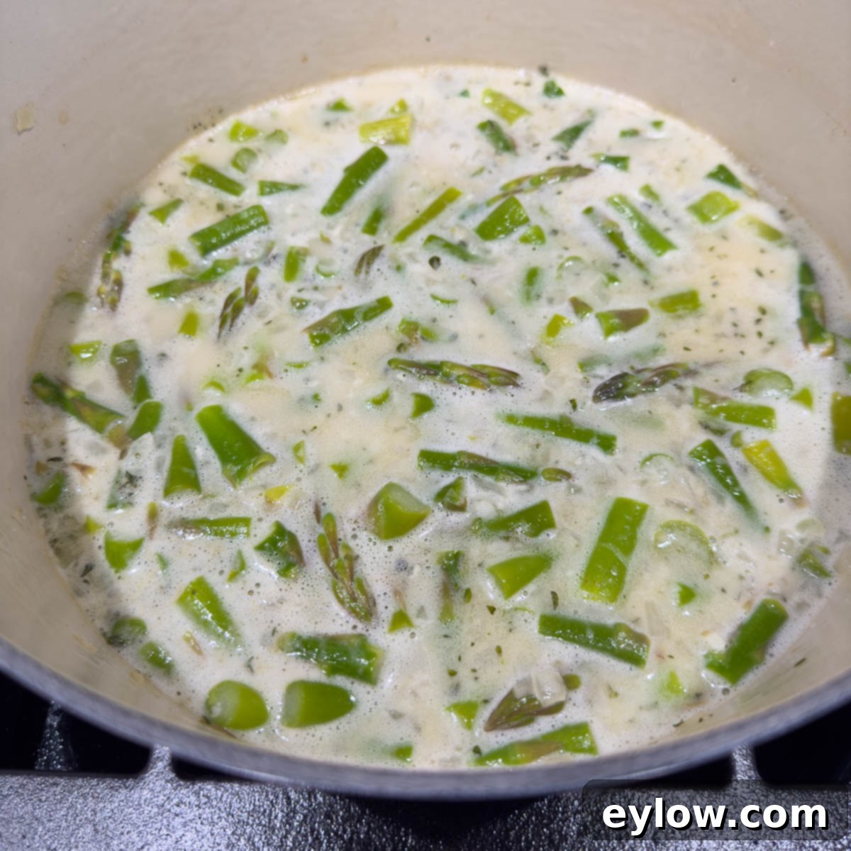 Adding broth and coconut milk to the pot with asparagus and aromatics for simmering.