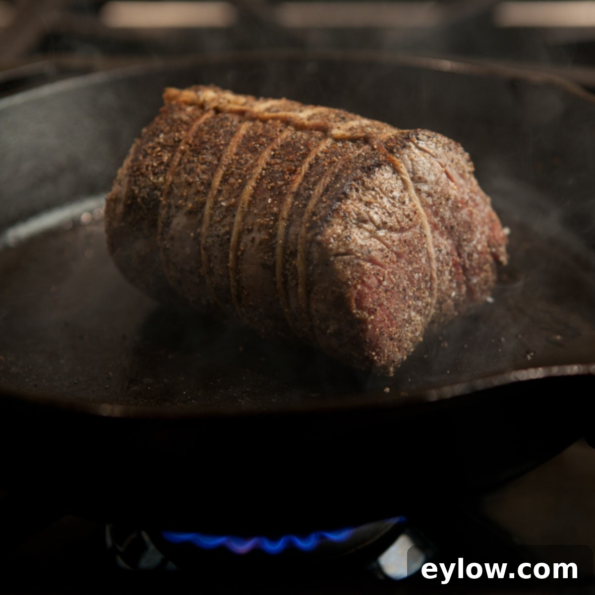 Beef tenderloin searing in a cast iron pan on the stove.