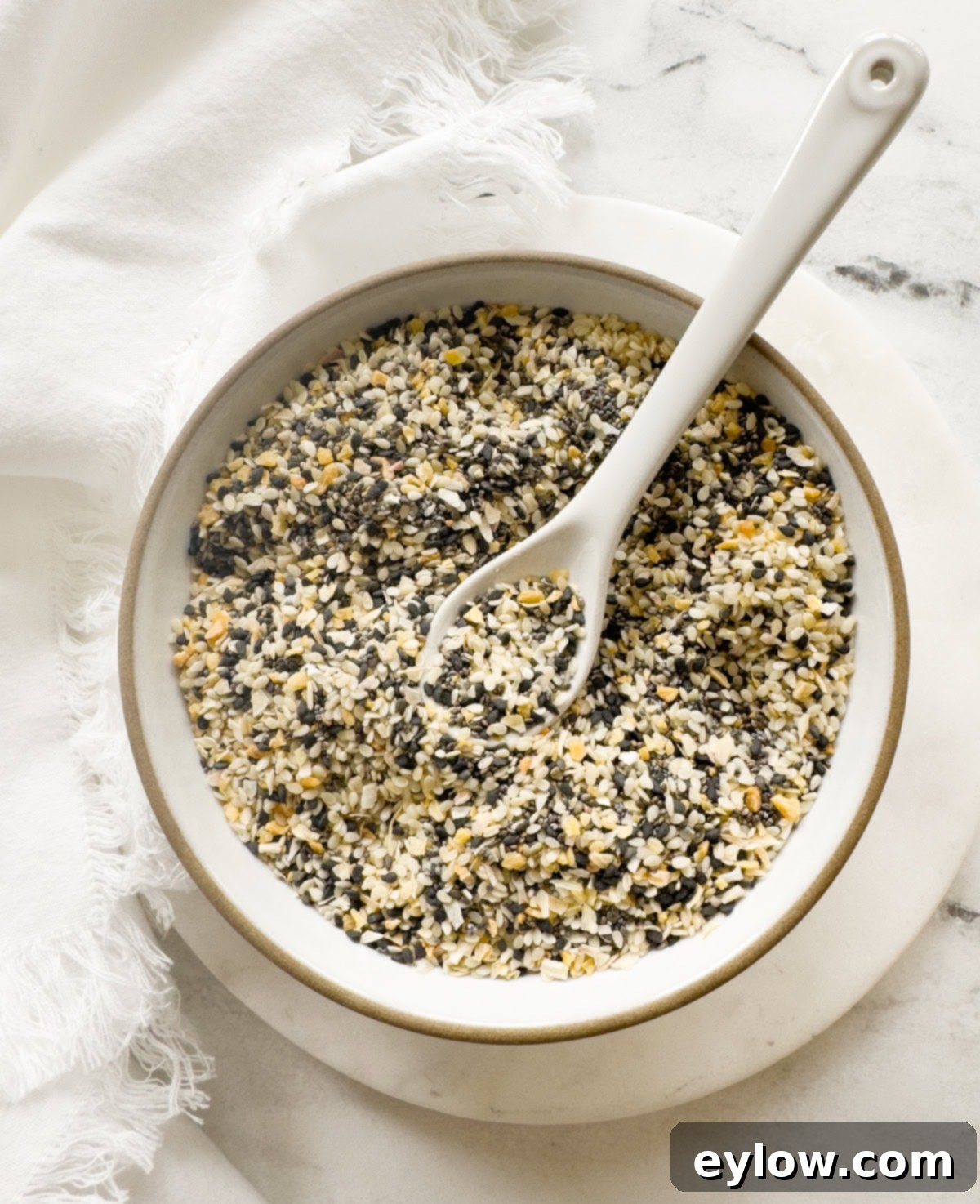 DIY Everything Bagel Seasoning 2 A small white bowl filled with homemade everything bagels seasoning and a white spoon.