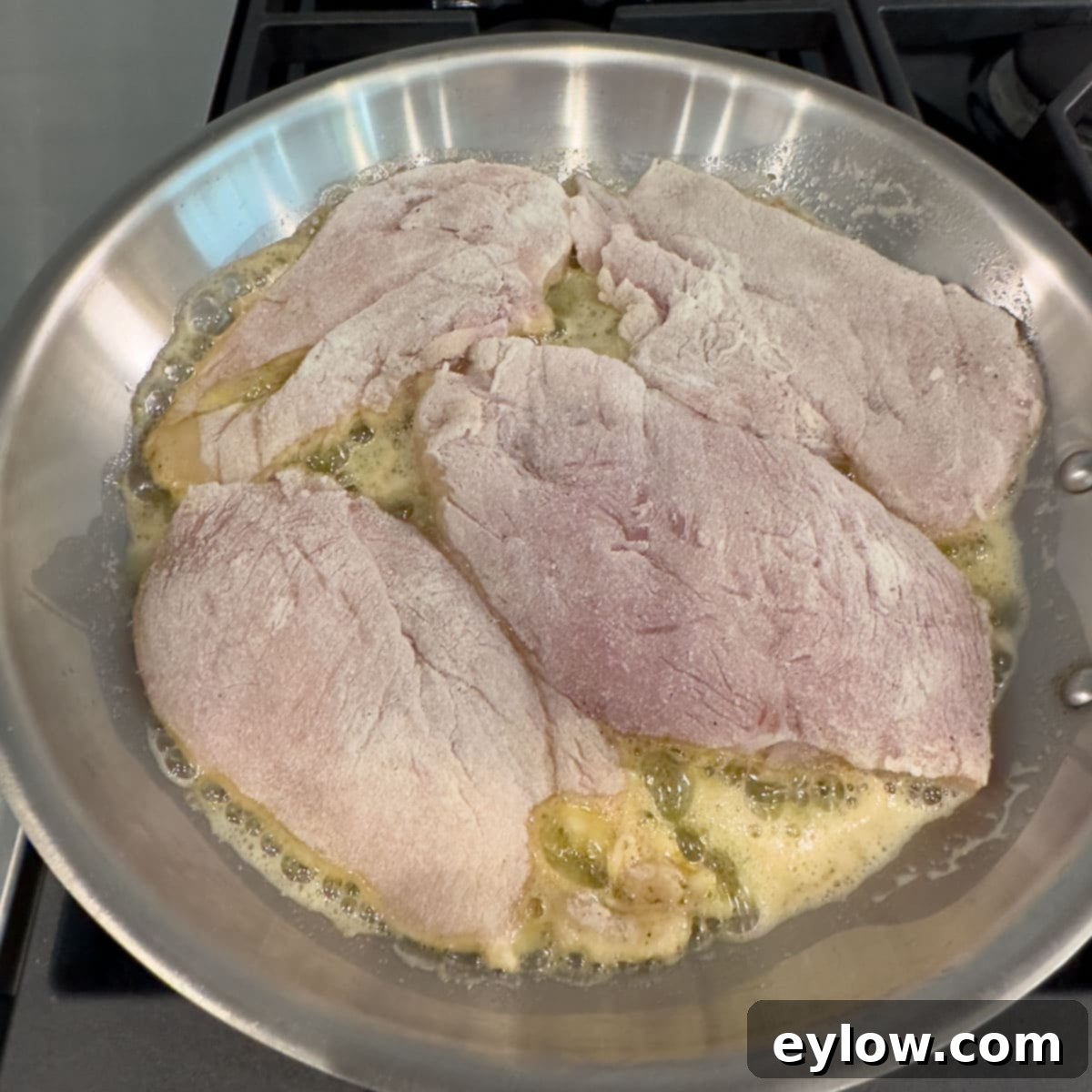 Cooking chicken cutlets in a stainless steel fry pan, showing the first side browning to a beautiful golden color.