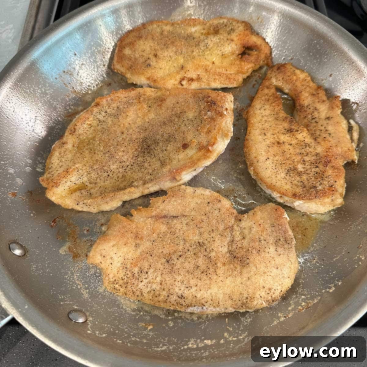 Golden-brown chicken cutlets perfectly cooked in a skillet, ready to be turned.