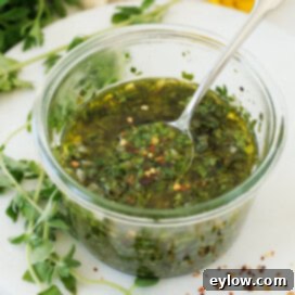 A jar of salsa chimichurri of parsley, oregano, olive oil, onion, and vinegar, highlighting the fresh, vibrant ingredients.