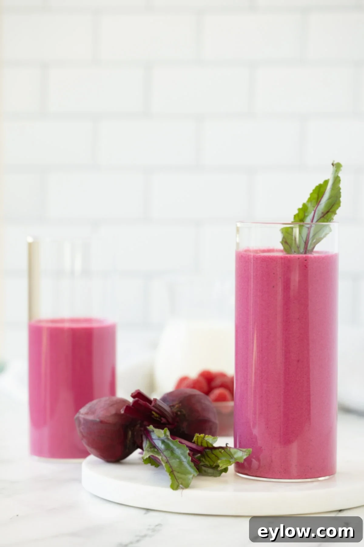A bright fuchsia colored red beet smoothie in tall glass with red beets on side.