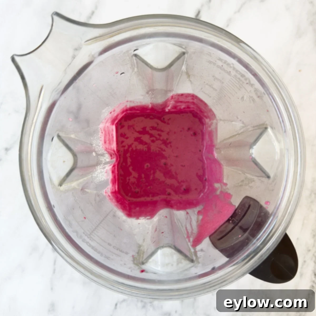 Bright pink smoothie with red bees and raspberries in a blender container, pureed.