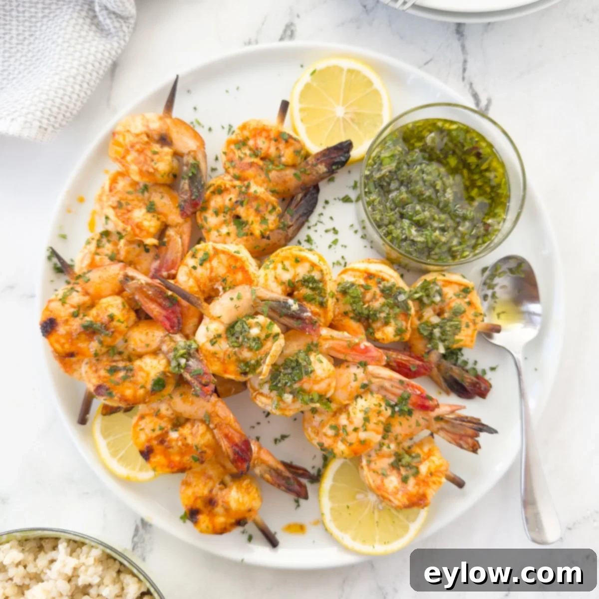 Grilled shrimp on bamboo sticks on a white platter with chimchurri sauce.