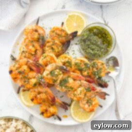 Grilled shrimp on bamboo sticks on a white platter with chimchurri sauce.