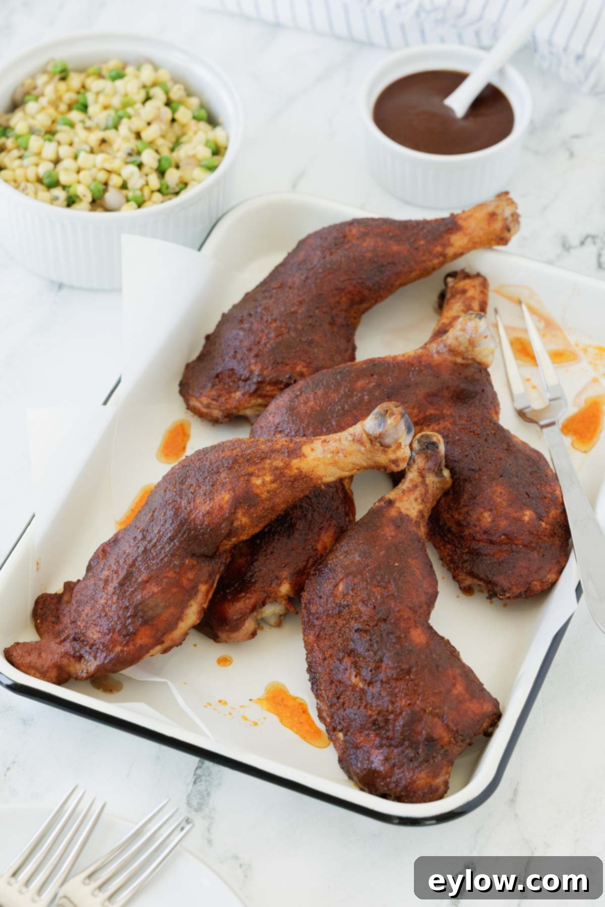smoked chicken legs on a white tray with parchment and a big silver serving fork.