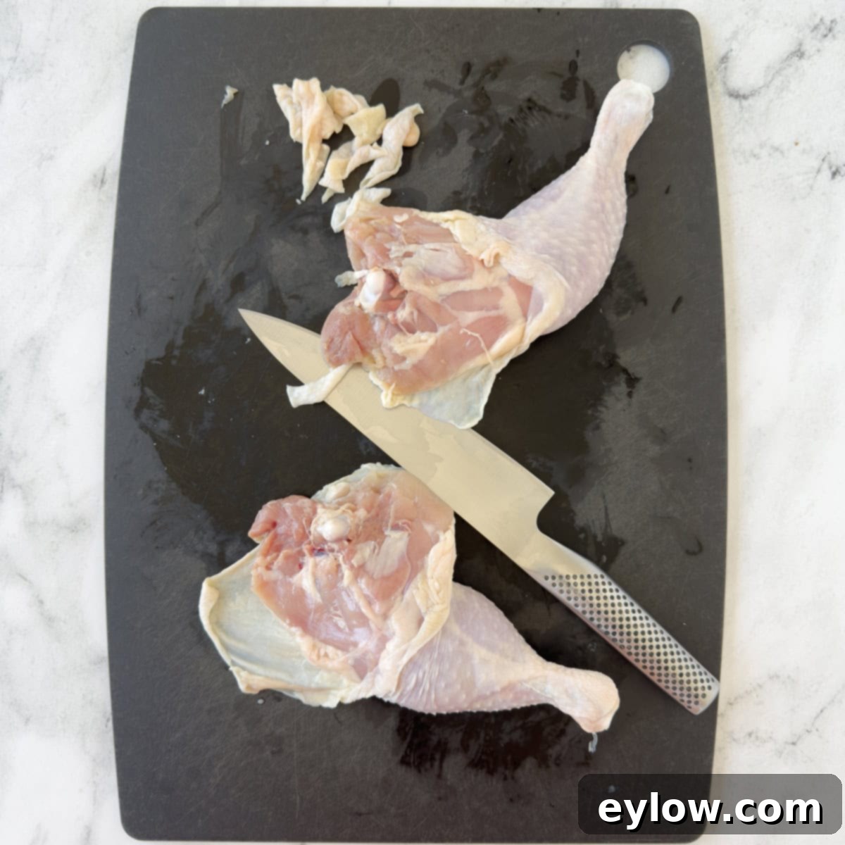 Trimming raw whole chicken legs of extra fat on a chtting board.