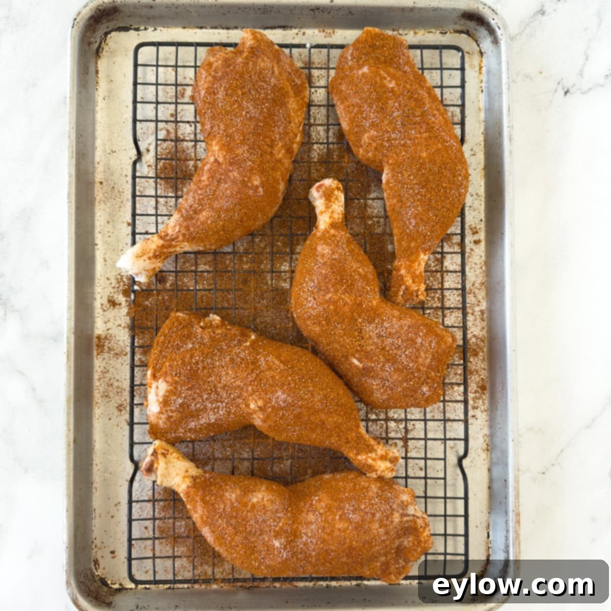 Seasoned chicken legs in a bright orange red dry rub on a wire rack and sheet pan.
