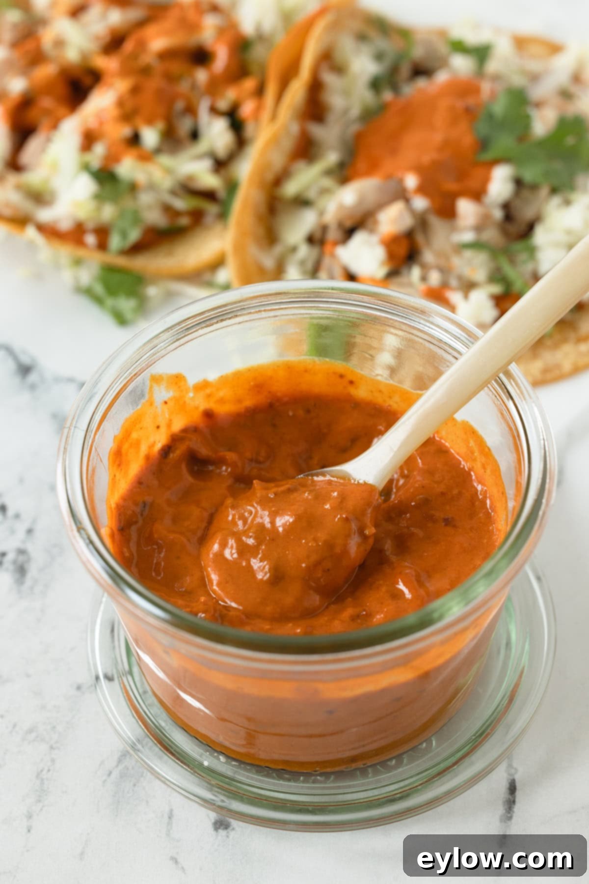 A jar of bright orange harissa aioli with tacos in the back.