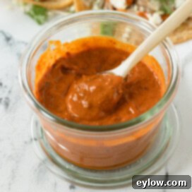 Chunky harissa aioli sauce in a jar with a cream colored spoon.