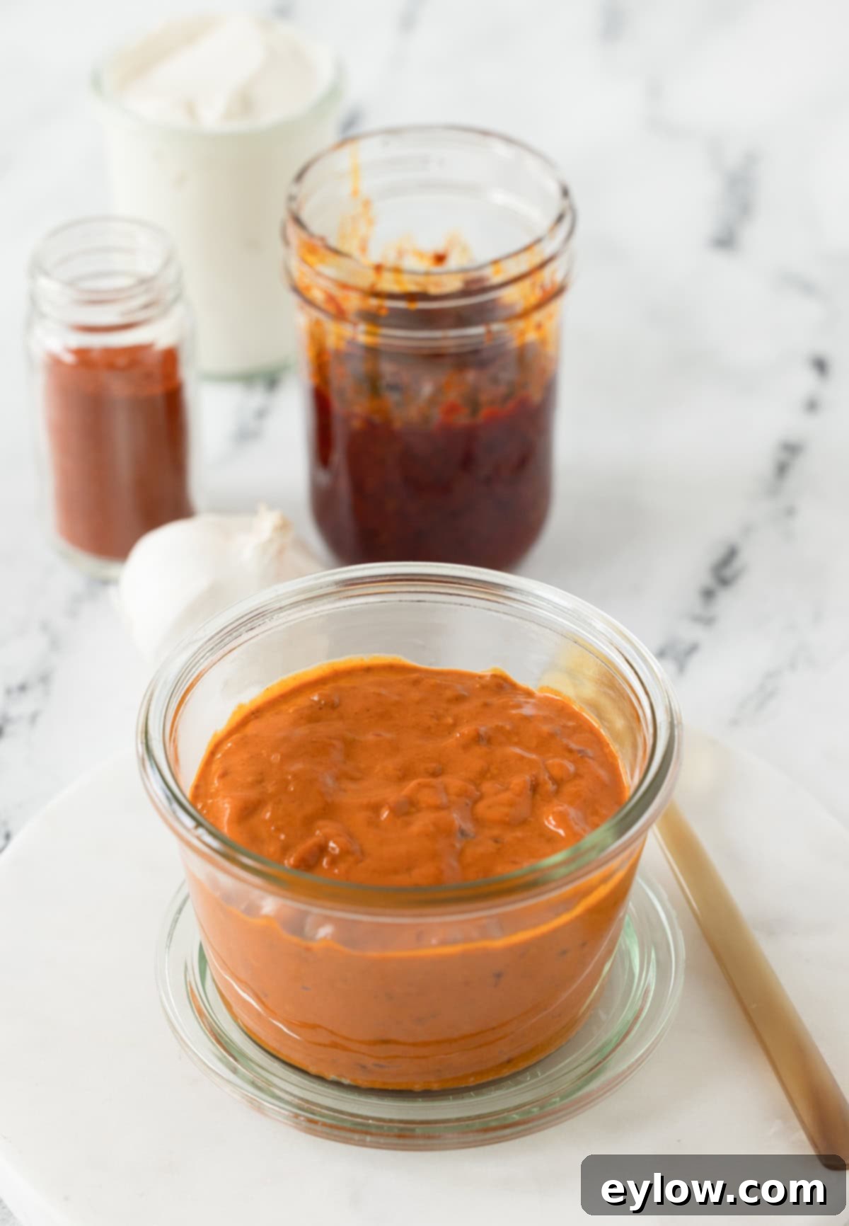 Bright orange harissa sauce ina jar with paprika, mayo, paste, and garlic.
