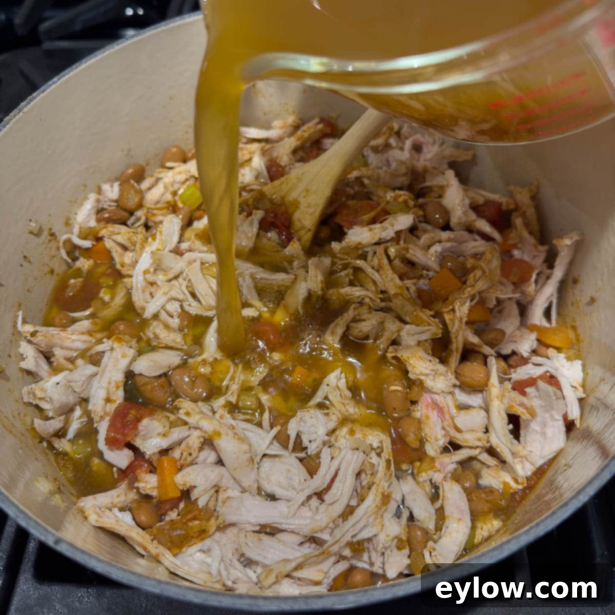 Adding shredded chicken and broth to the pot to complete the soup.
