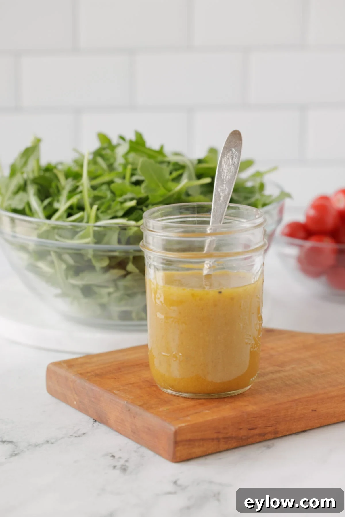A jar of classic French vinaigrette dressing with a silver spoon and fresh salad greens in the background, ready to be served.