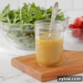 Small glass jar on a kitchen counter of French vinaigrette with salad behind.