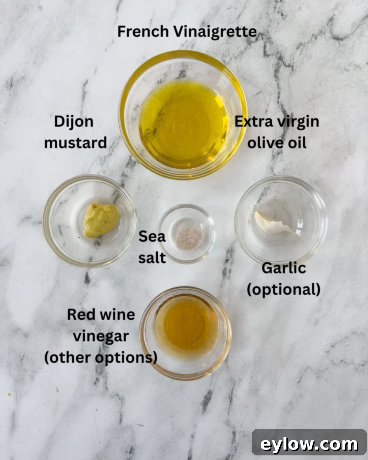 A collection of ingredients for a French vinaigrette salad dressing, neatly arranged in small prep bowls, showcasing olive oil, red wine vinegar, Dijon mustard, and a garlic clove.