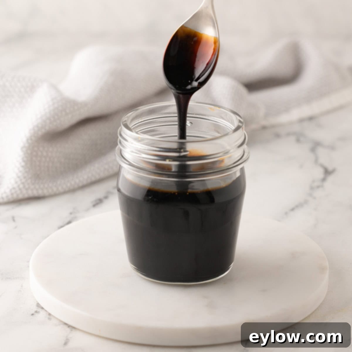 Burrata Peach and Prosciutto Summer Salad 5 Balsamic glaze dripping off a silver and gold spoon into a glass jar.