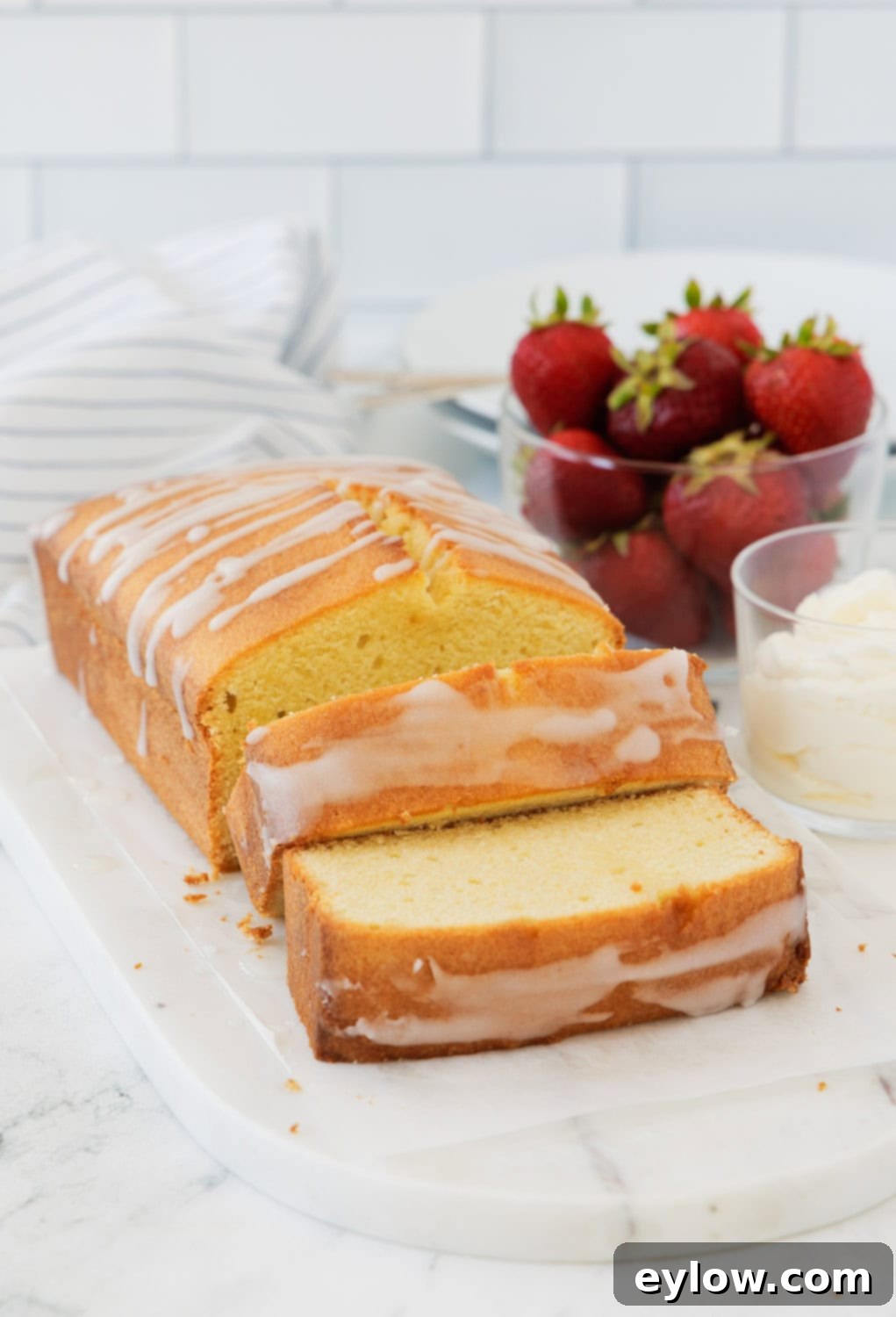 Artisan Gluten-Free Cream Cheese Pound Cake 14 Sliced pound cake ona marble board with strawberries and whipped cream on the side.