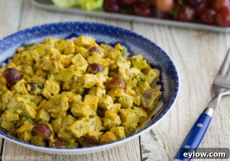 Golden curried chicken salad in a blue bowl with blue fork, garnished and ready for a healthy meal.