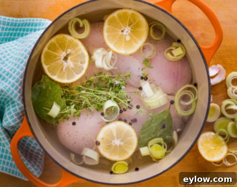 Boneless skinless chicken breasts poaching in a pot of water on the stove.