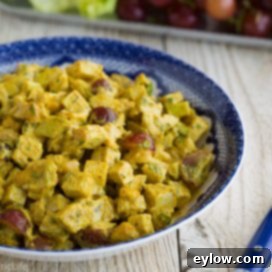 Close-up of golden curried chicken salad in a serving bowl with a blue fork.