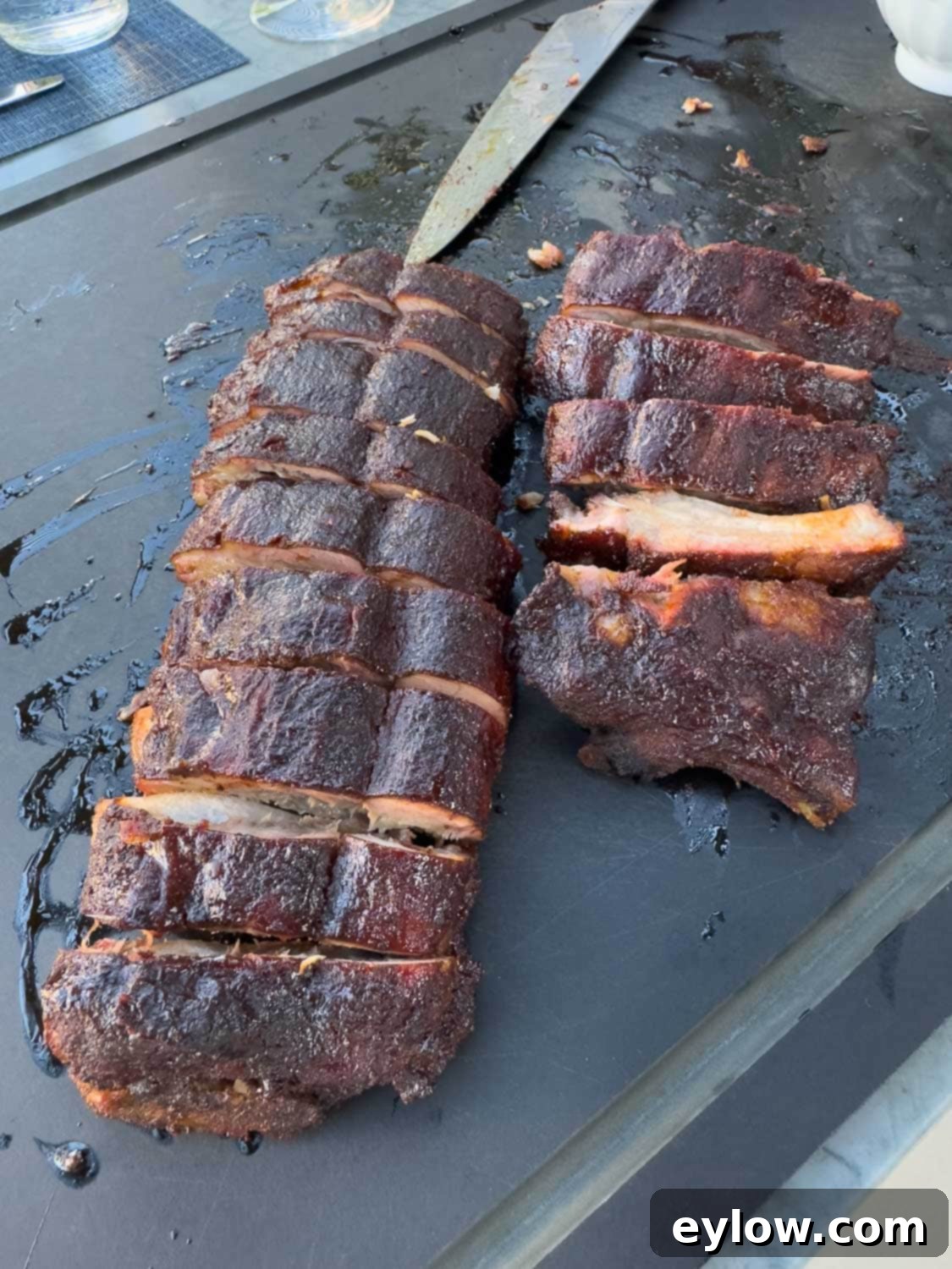 Sliced, smoked baby back ribs on a black cutting board outside by the grill.