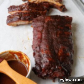 Smoked baby back ribs being sliced on a sheet tray with BBQ sauce.