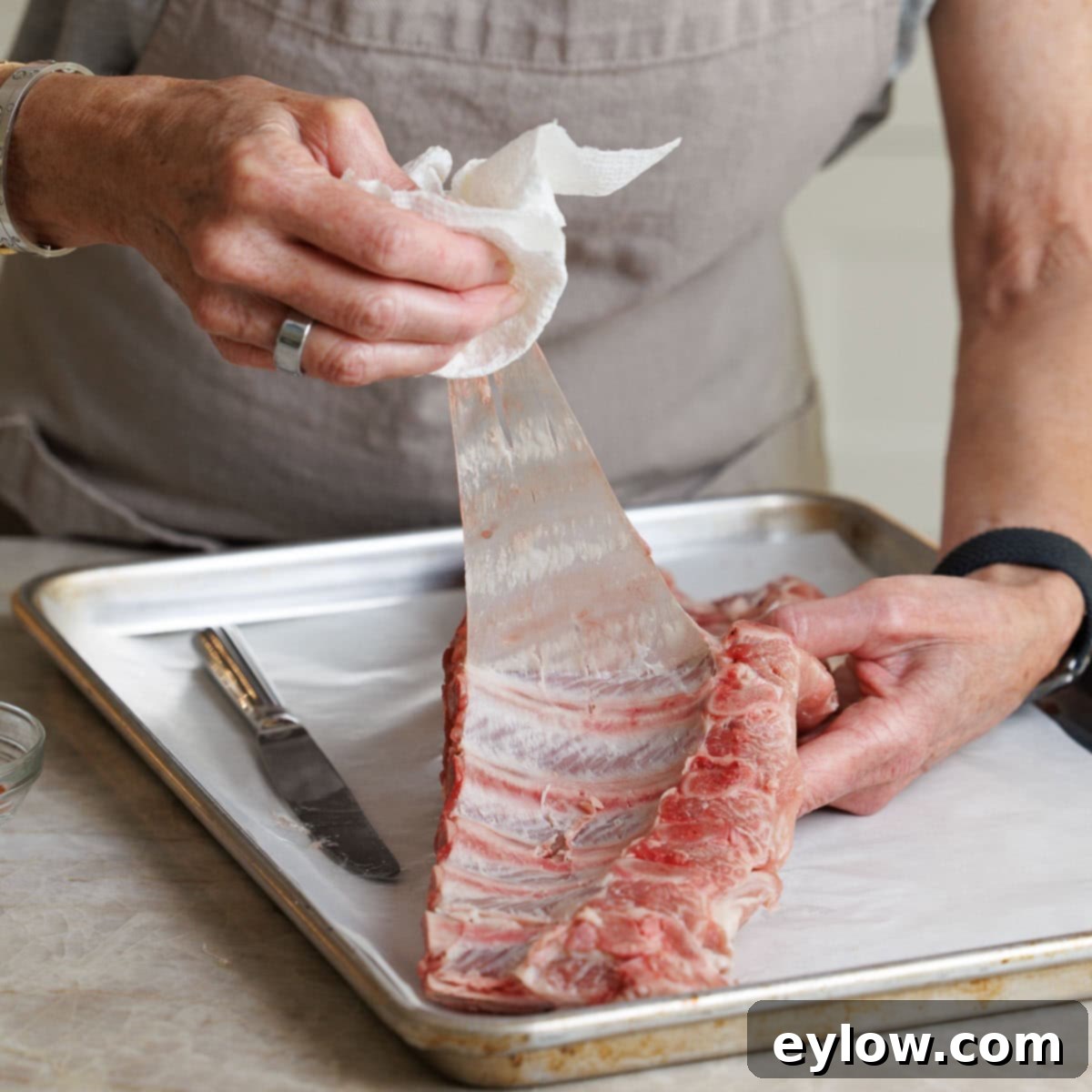 Pulling off the silver skin from a rack of ribs with a paper towel.