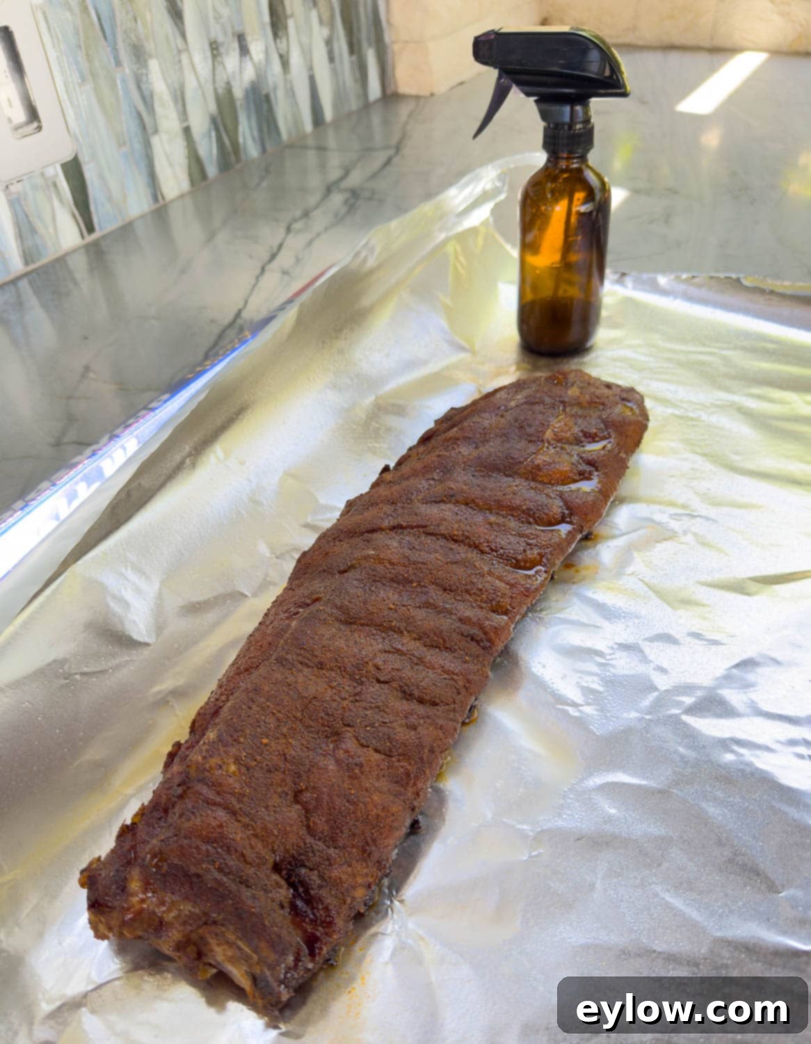 Smokes baby back ribs on a large piece of foil with a rib spritz bottle ready for wrapping. 