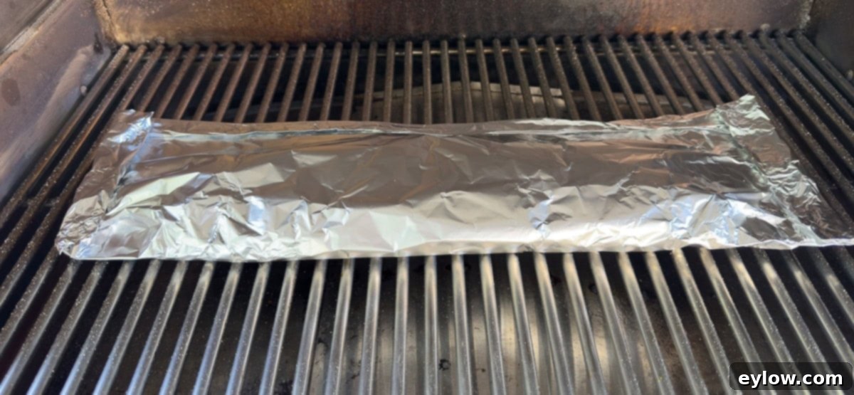 Ribs wrapped in a foil packet for phase two of smoking, on grill grates. 