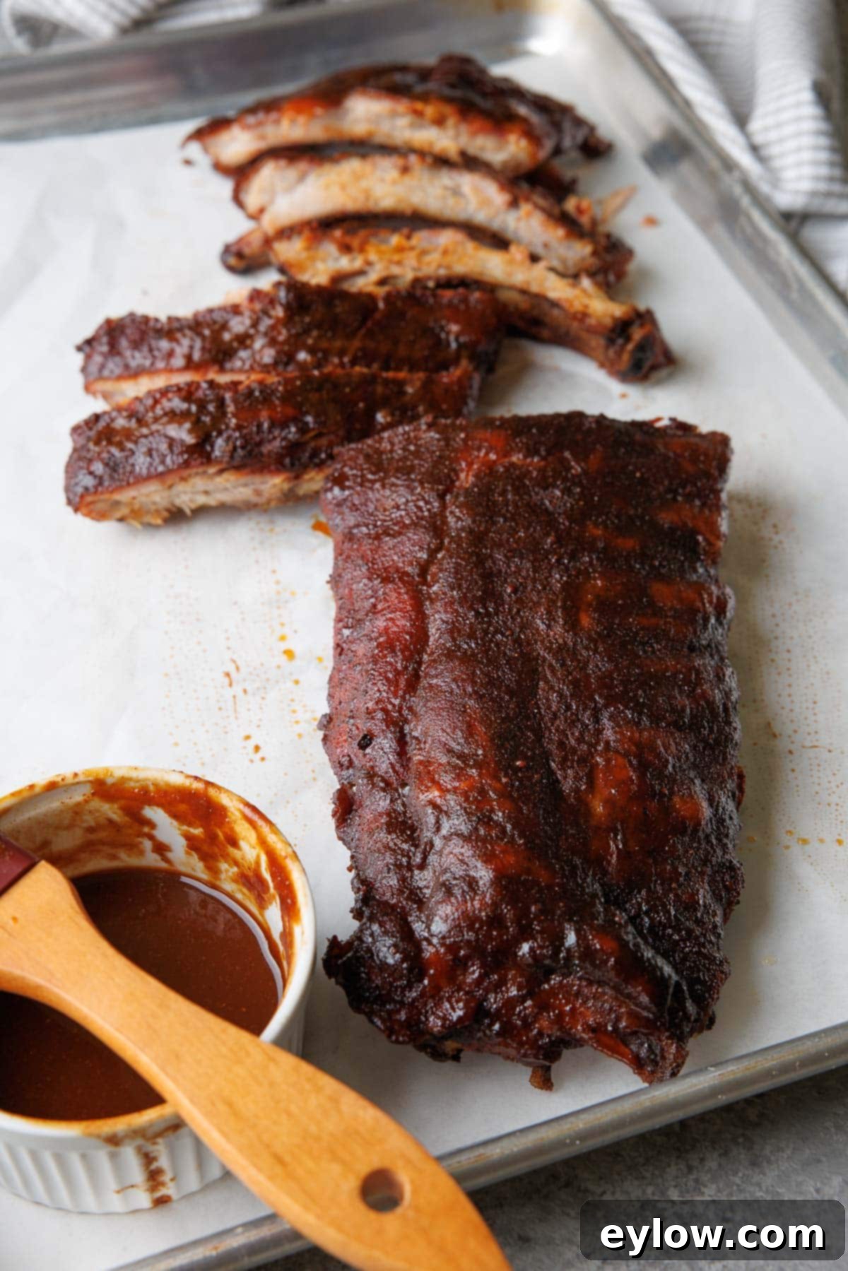 smoked baby back ribs with a few sliced on a sheet tray with bbq sauce.
