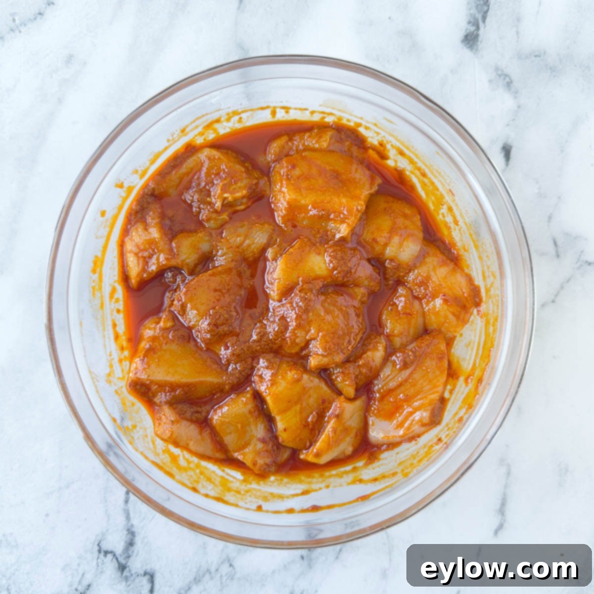 Fiery Harissa Chicken Skewers 5 Pieces of chicken breast submerged in a vibrant orange harissa marinade within a clear glass bowl, ready for marinating.