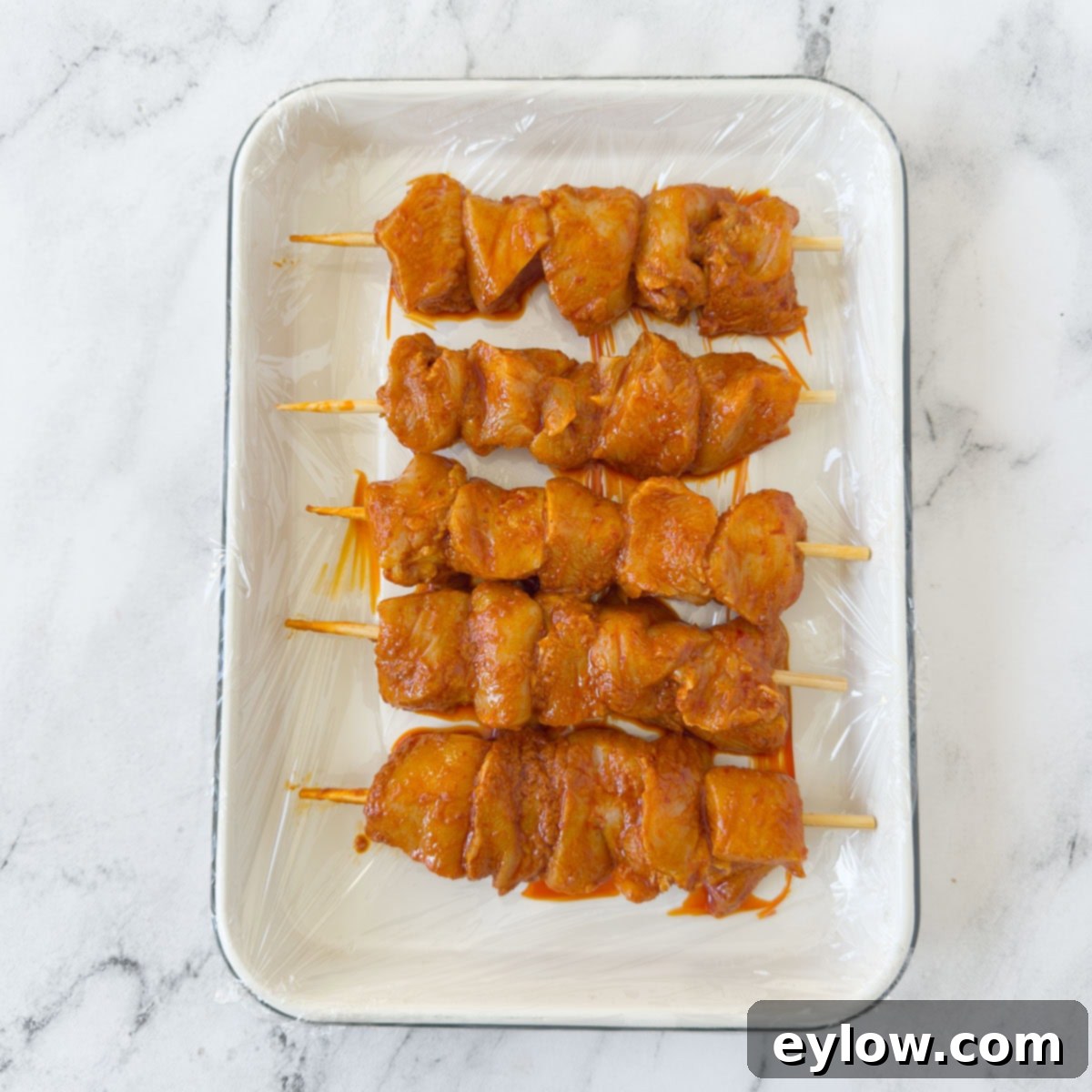 Fiery Harissa Chicken Skewers 7 Chunks of harissa-marinated chicken threaded neatly onto bamboo skewers, arranged on a tray, ready for grilling.