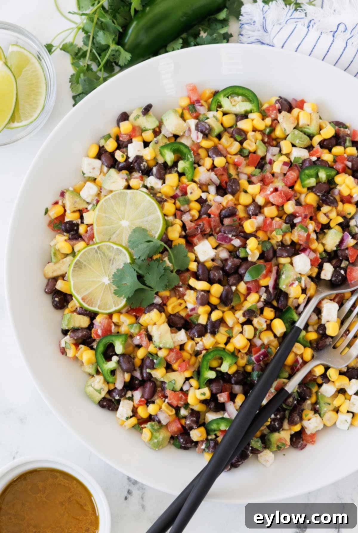 Vibrant avocado, corn, and black bean salad elegantly presented in a white serving bowl, accompanied by a serving spoon and fork, ready to be enjoyed.