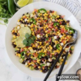 Bright colored avocado , black bean, and corn salad with tomatoes and jalapenos in a white bowl.