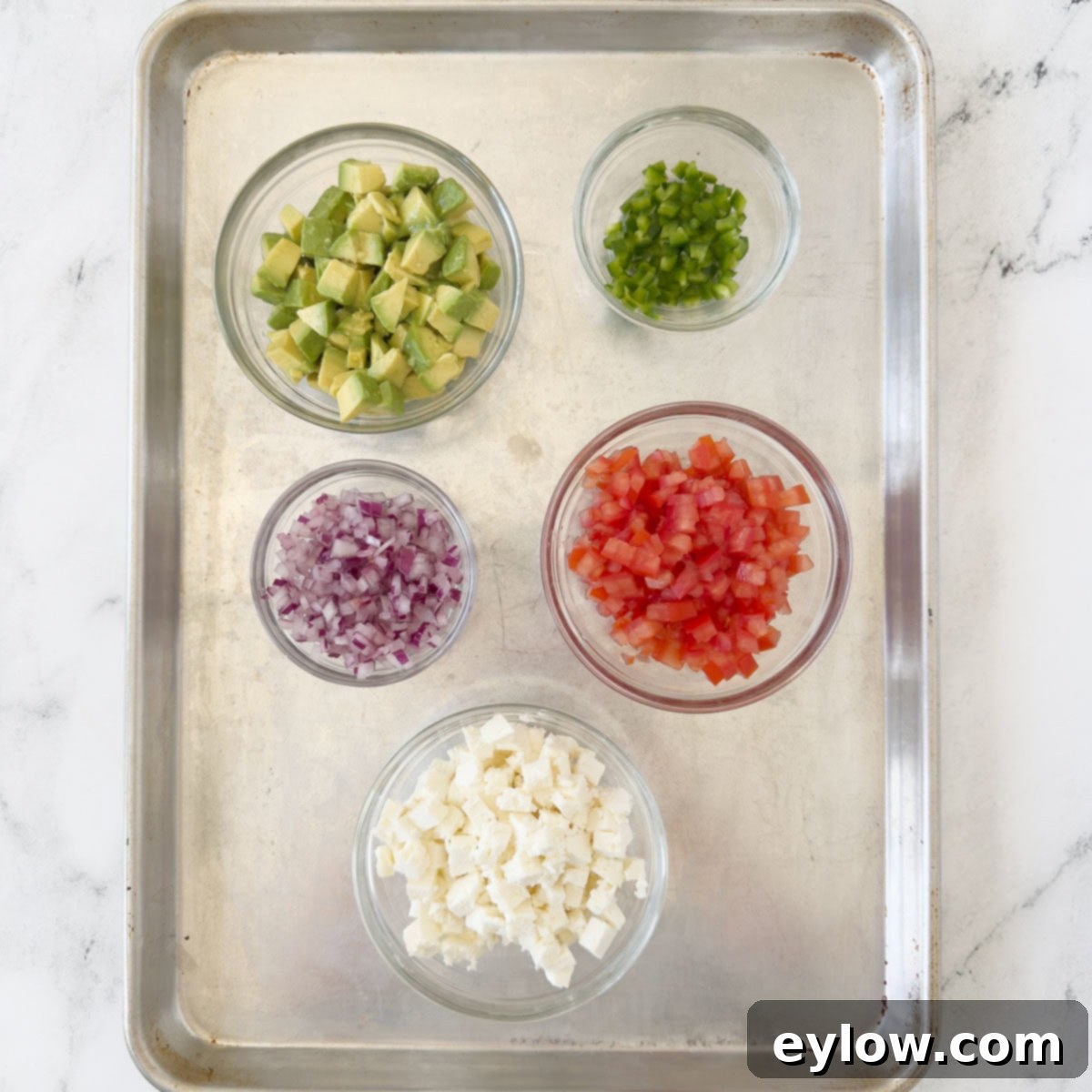 A vibrant assortment of freshly chopped avocado, ripe tomatoes, diced peppers, finely minced red onion, and crumbled feta cheese, ready for a salad.