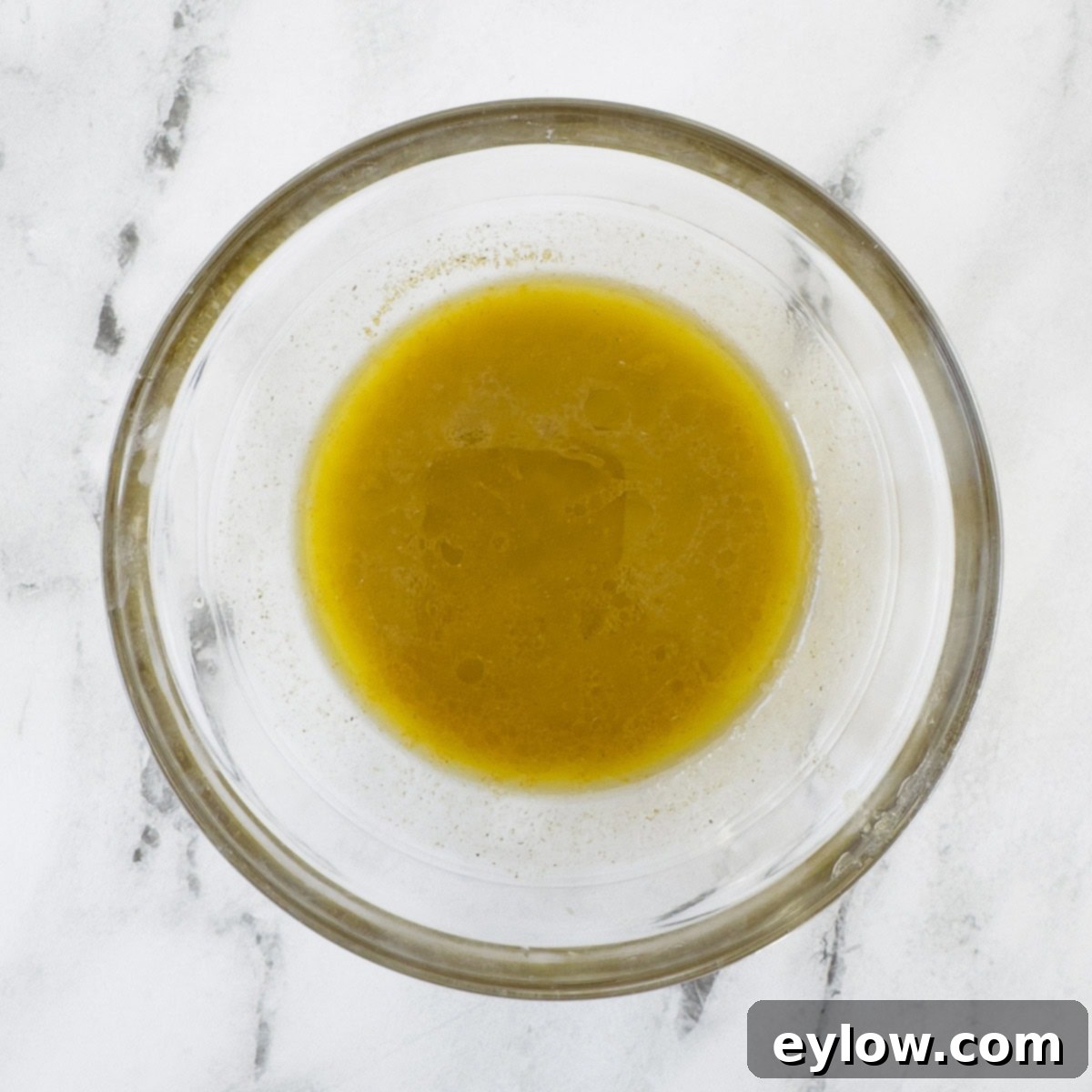 A small glass bowl filled with a shimmering golden yellow vinaigrette, perfectly emulsified and ready to dress a salad, resting on a clean counter.