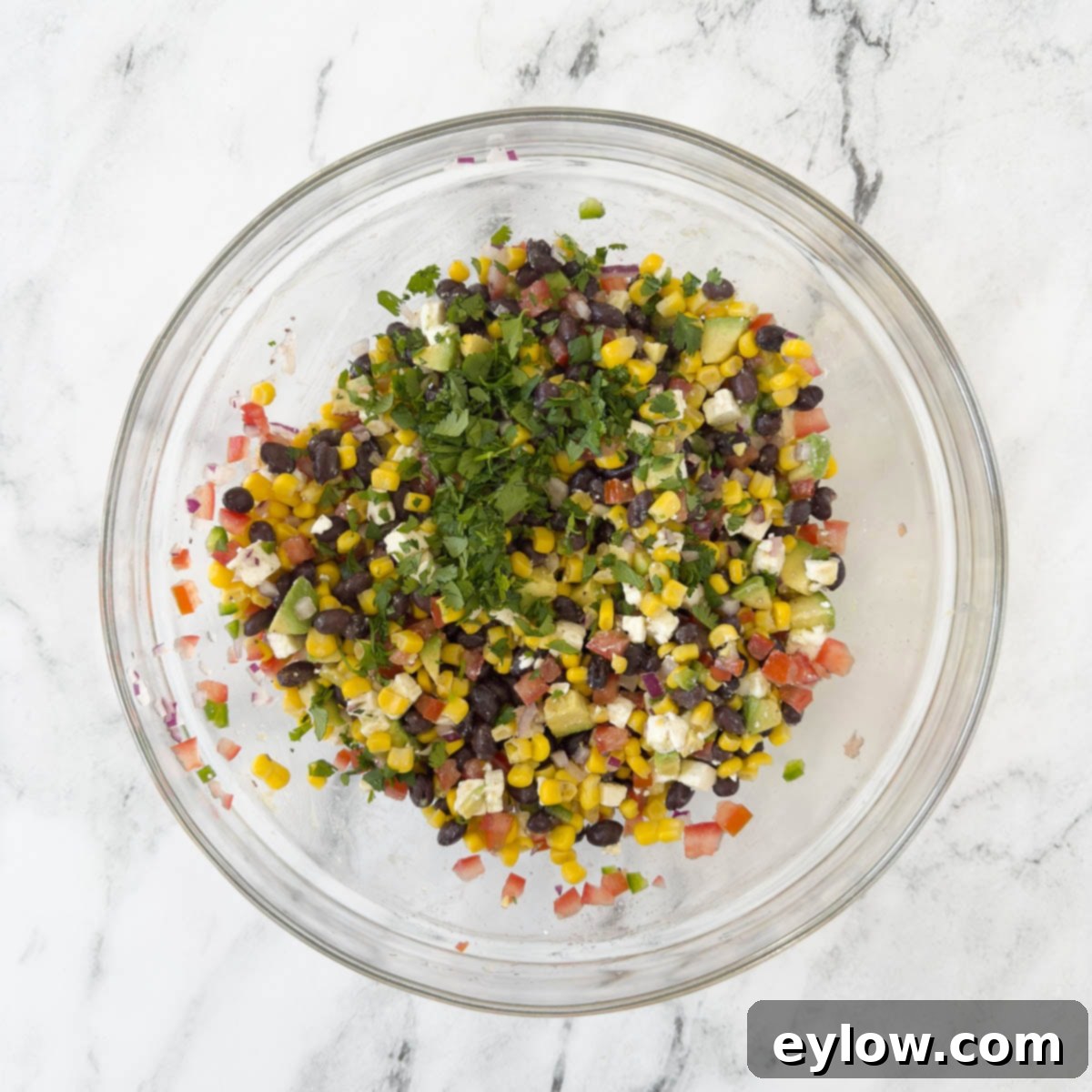 A close-up shot of a vibrant black bean, corn, and avocado salad being gently mixed in a large bowl, showcasing its colorful ingredients.