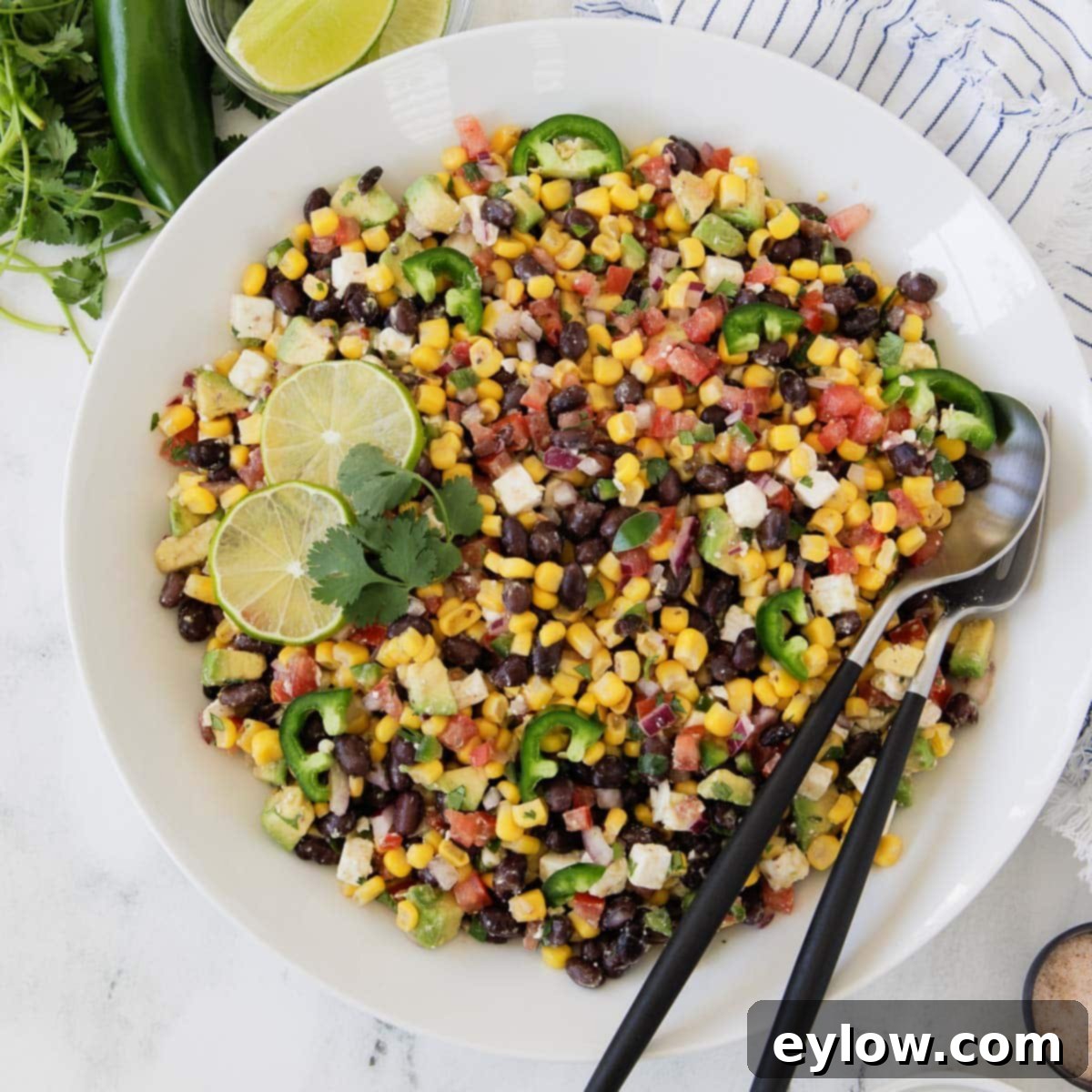 A bright, colorful and appetizing avocado, black bean, and corn salad, garnished with tomatoes and jalapeños, served in an elegant white bowl.