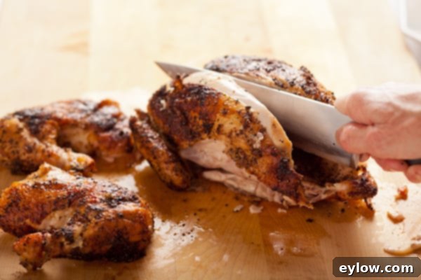 A perfectly roasted whole chicken, expertly carved, with its tender meat and crispy skin visible on a wooden cutting board, ready for serving.