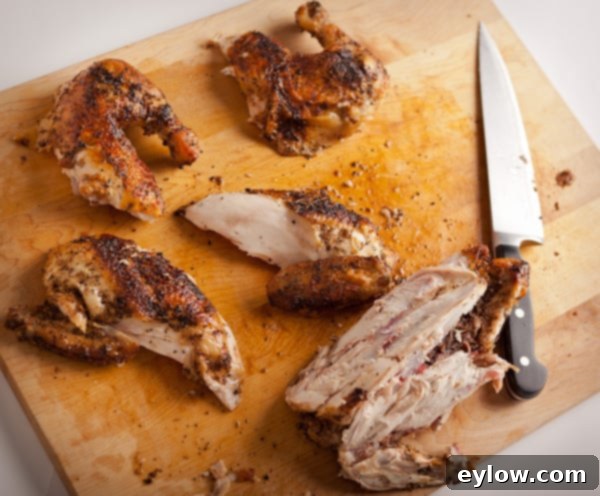 Close-up view of carving a whole roast chicken on a cutting board, highlighting the juicy breast meat being separated from the bone.