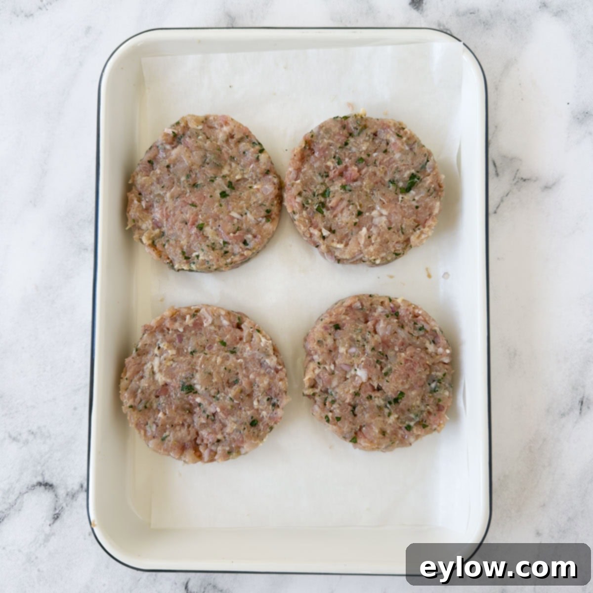 Homemade Air Fryer Chicken Patties 5 Formed raw chicken patties ready for the air fryer on a white pan.
