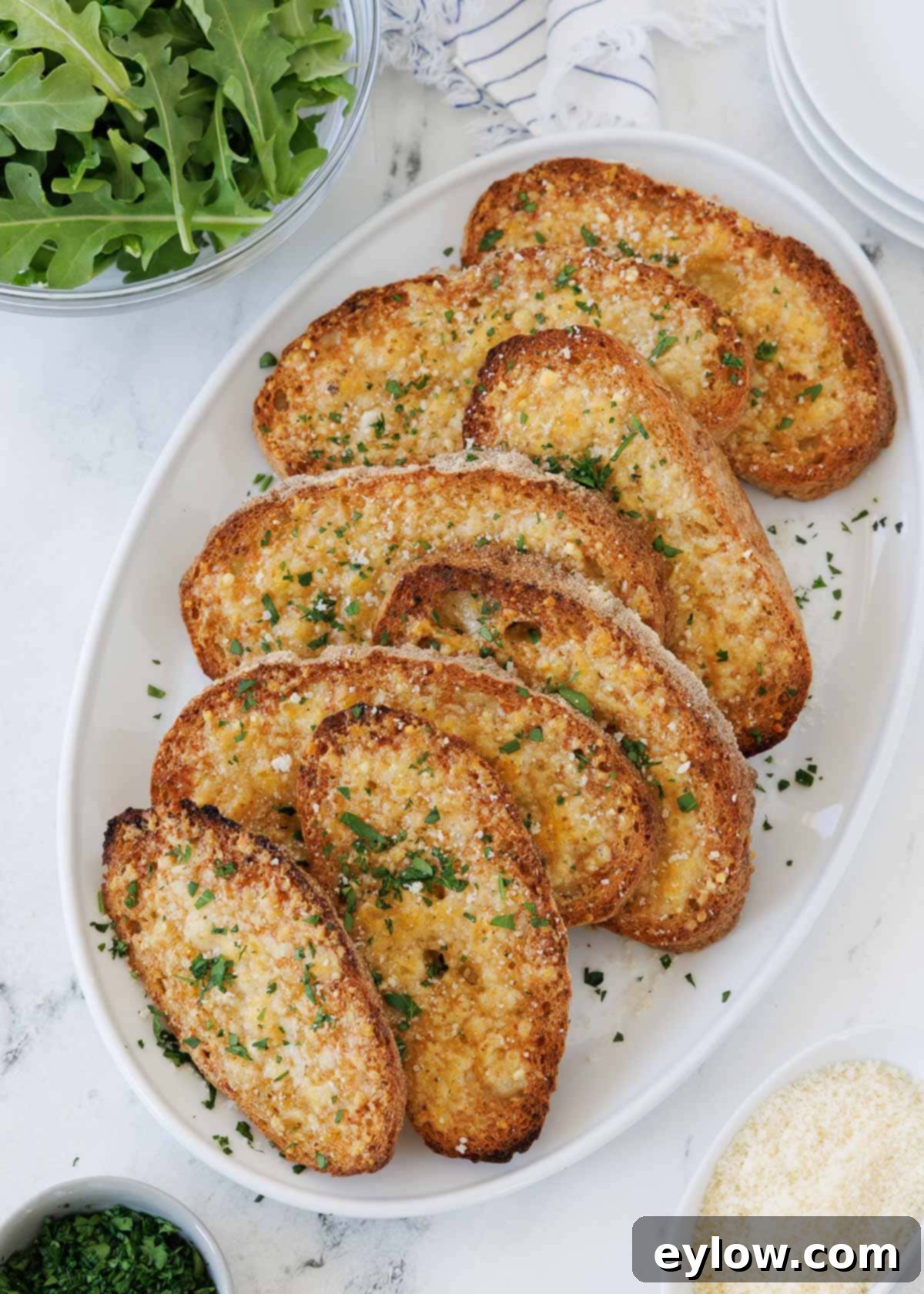 An oval plate of cheesy golden garlic toast sprinkled with parmesan and fresh parsley, ready to be served.