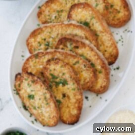 Golden cheesy gluten free garlic toast on a platter, garnished with fresh parsley.