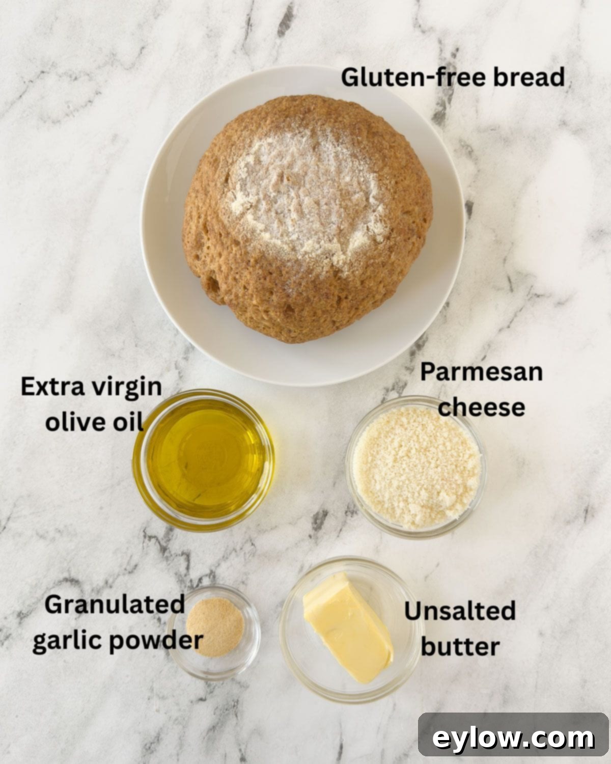 Ingredients for gluten-free garlic bread laid out on a marble counter, including bread, butter, olive oil, garlic powder, and Parmesan cheese.