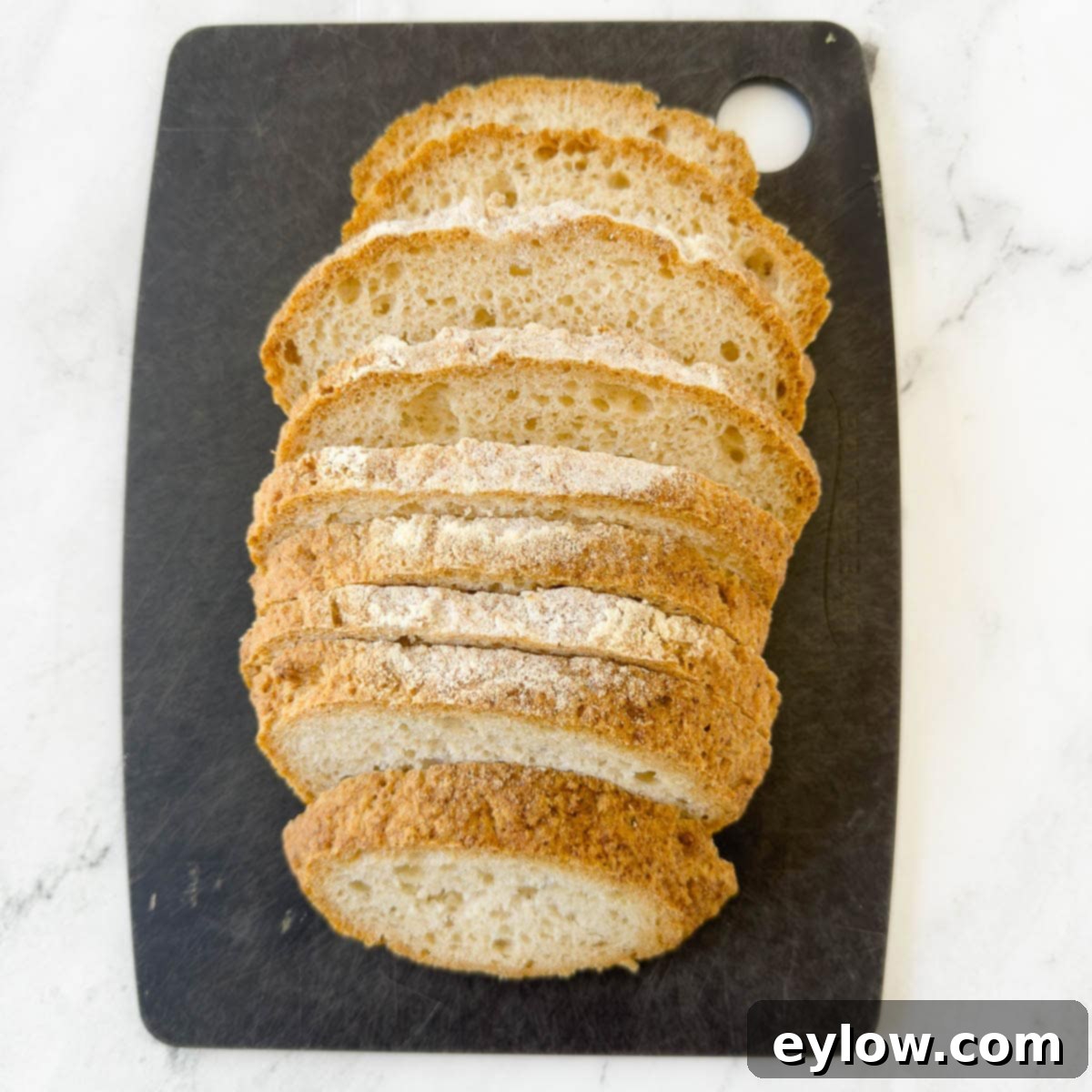 A loaf of artisan gluten-free bread perfectly sliced into 1-inch thick pieces on a black cutting board.