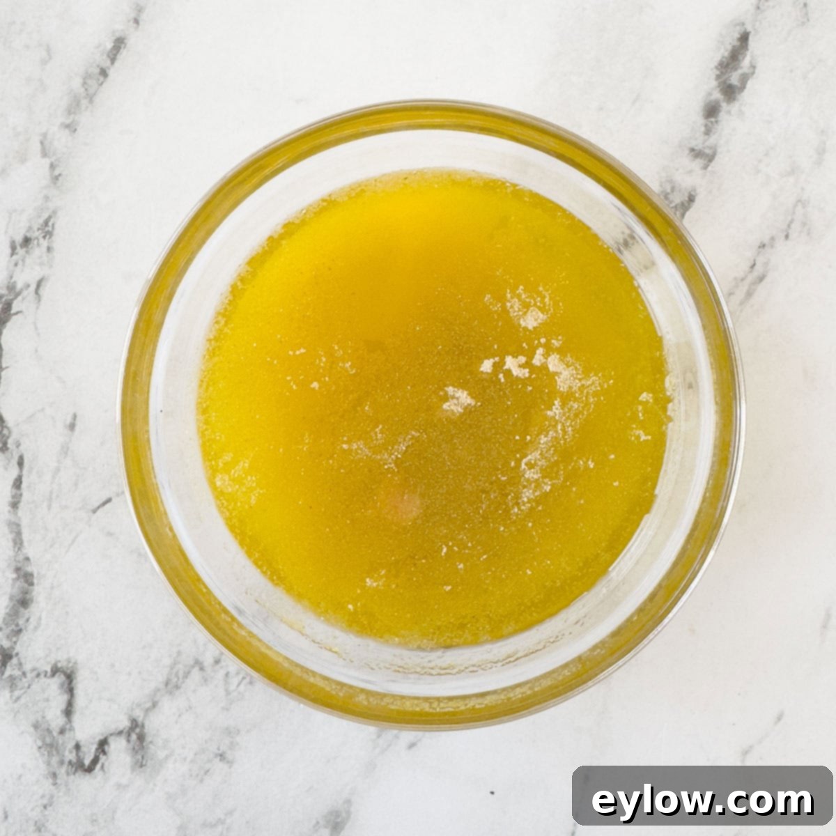 Olive oil, unsalted butter, and granulated garlic powder melted together and stirred in a small clear glass bowl.