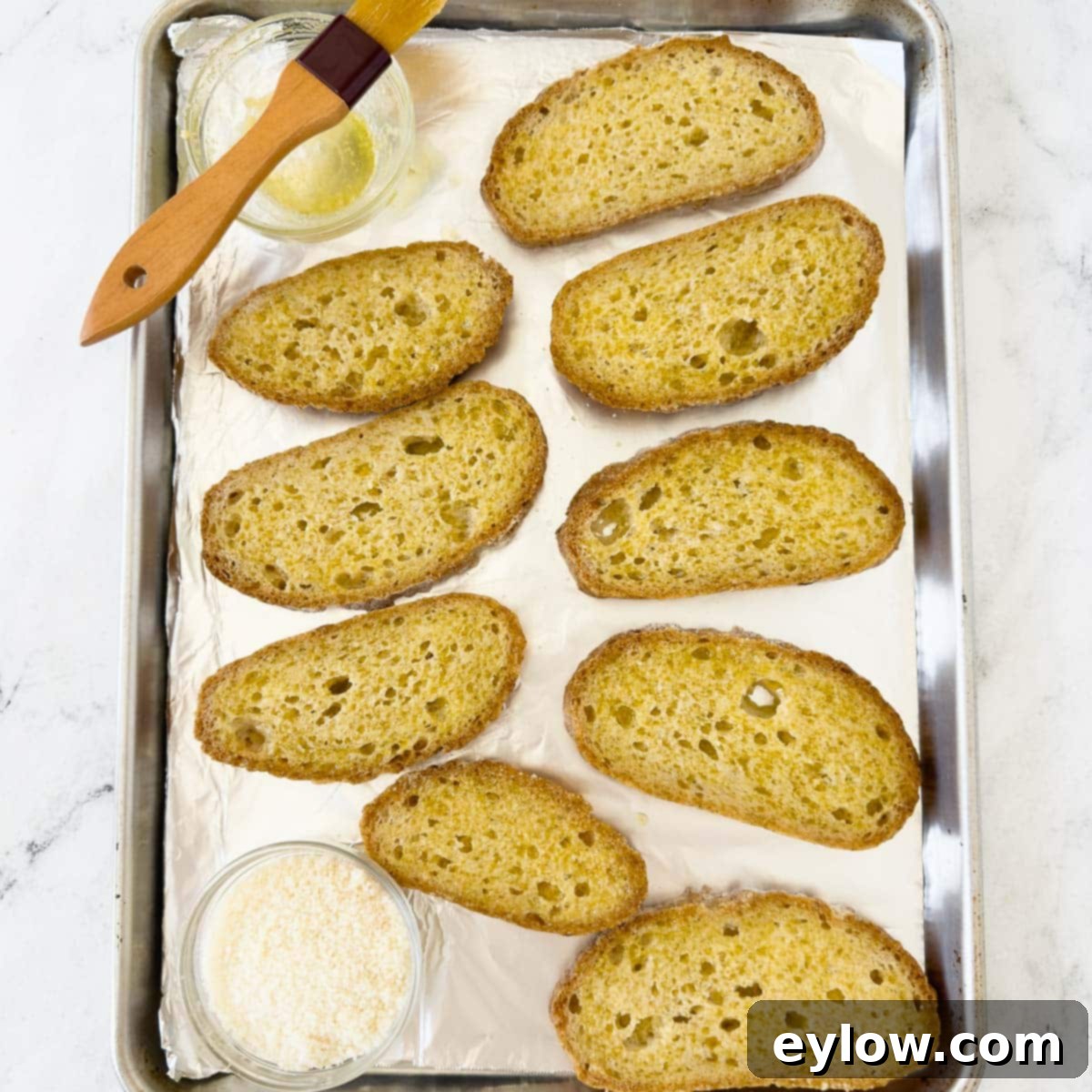 Slices of gluten-free bread arranged on a baking sheet, each generously brushed with the olive oil and garlic butter mixture.